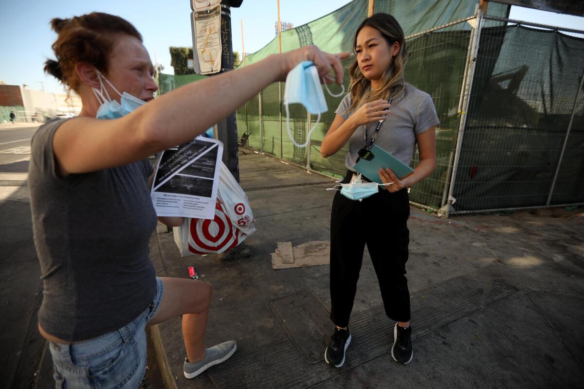 A woman listens to another woman speak while standing on a sidewalk