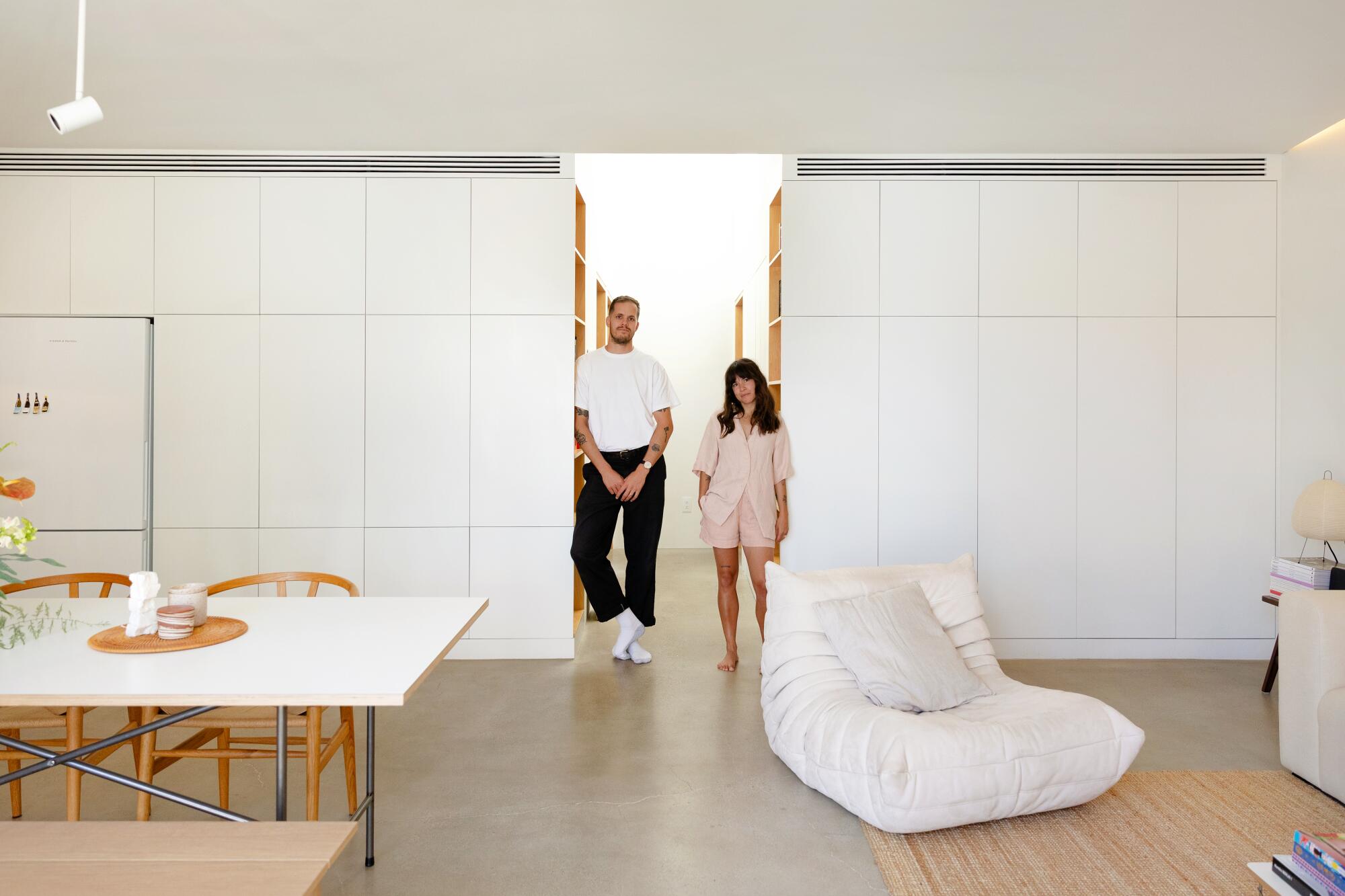A man and a woman stand in an open-concept living area with white walls