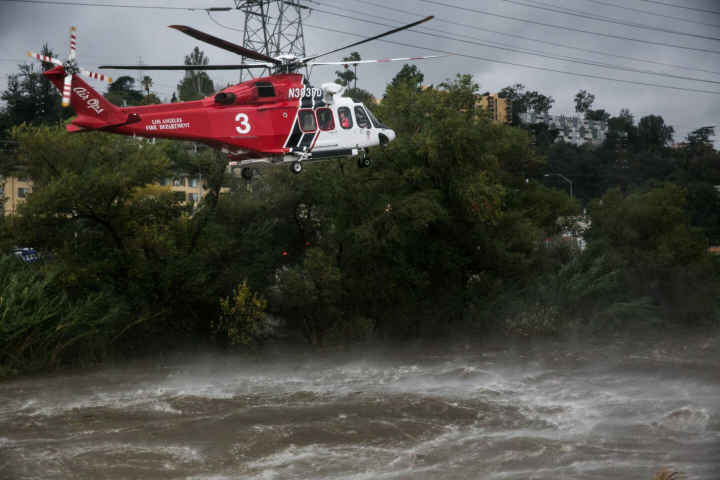 An L.A. Fire Department rescue helicopter flies low over the storm-swollen Los Angeles River in search of people in the water.