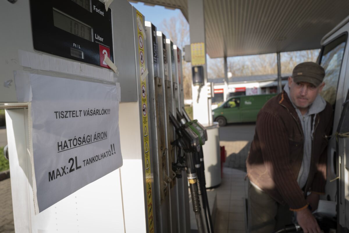 A driver fills up his car while sign on pump reads 'Dear Costumers! You can purchase only 2 liters of fuel at the regulated price!' in Martonvasar Hungary, Thursday, Dec. 1, 2022. Drivers in Hungary are running into fuel shortages at filling stations as a government-imposed price cap on fuel squeezes independent stations and leaves the state energy company struggling to keep up with demand. (AP Photo/Bela Szandelszky)