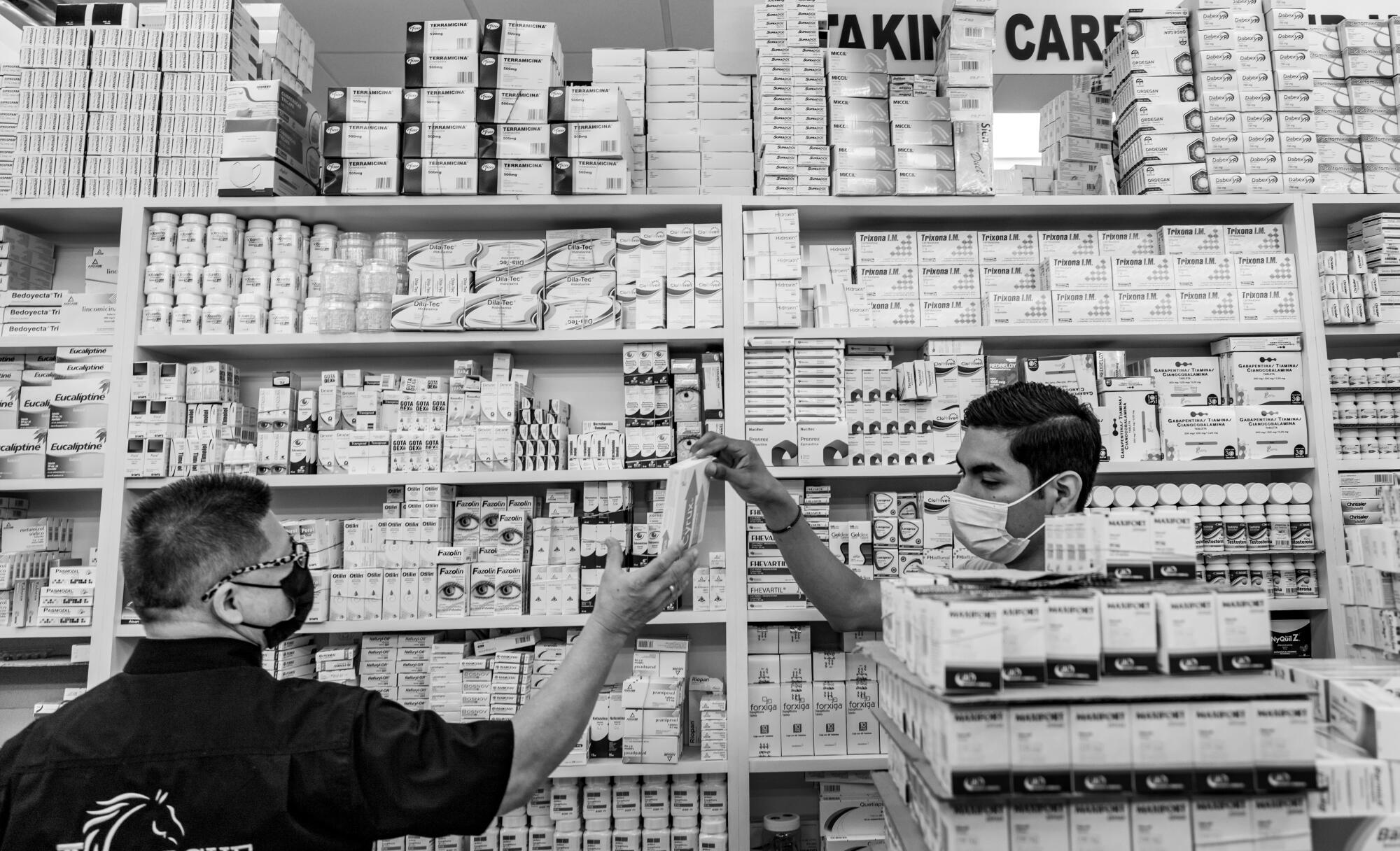 Pharmacy workers retrieve pills from a shelf 