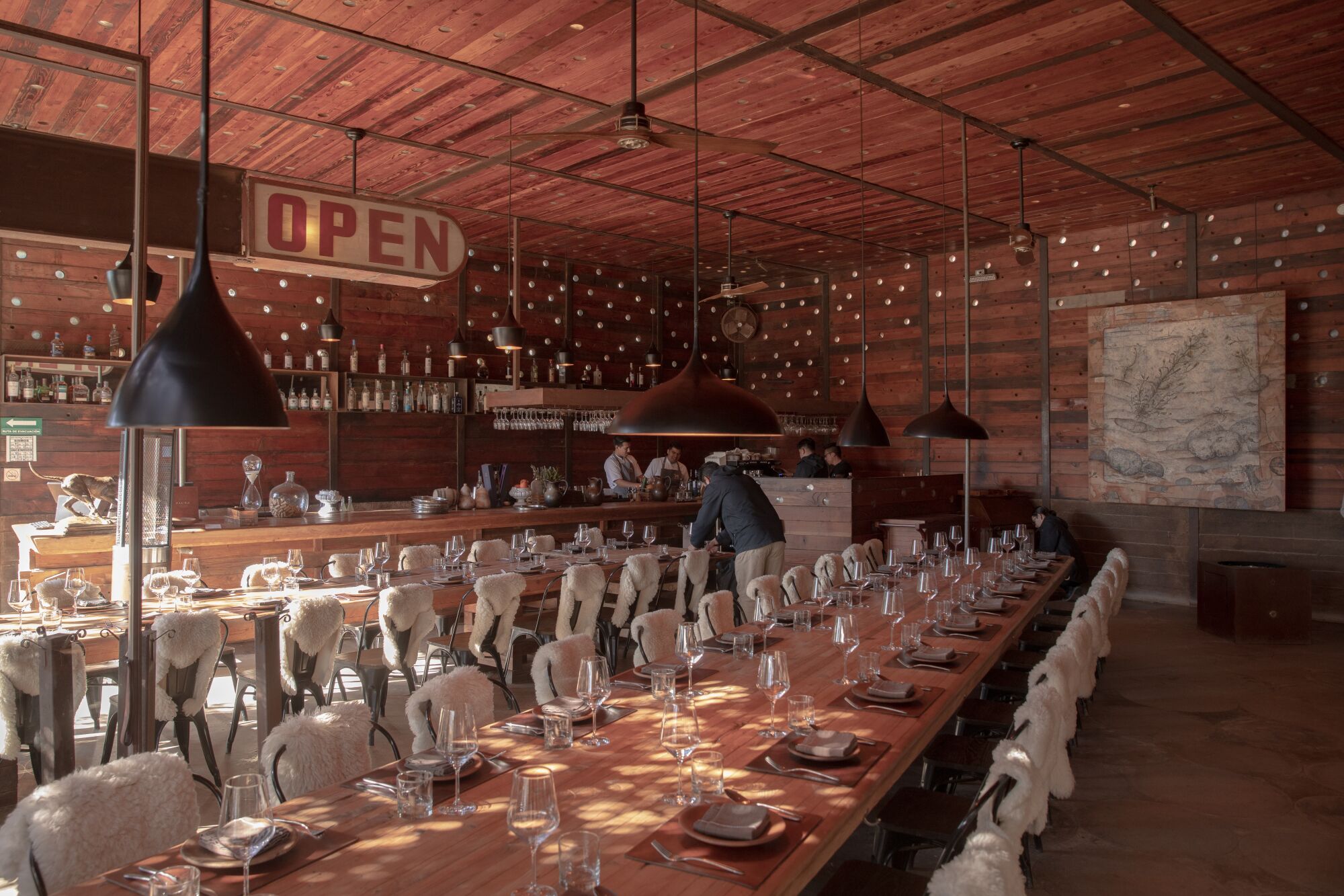 Two long dining tables set with plates and glasses, inside a restaurant with wood panelling in rich shades of brown.