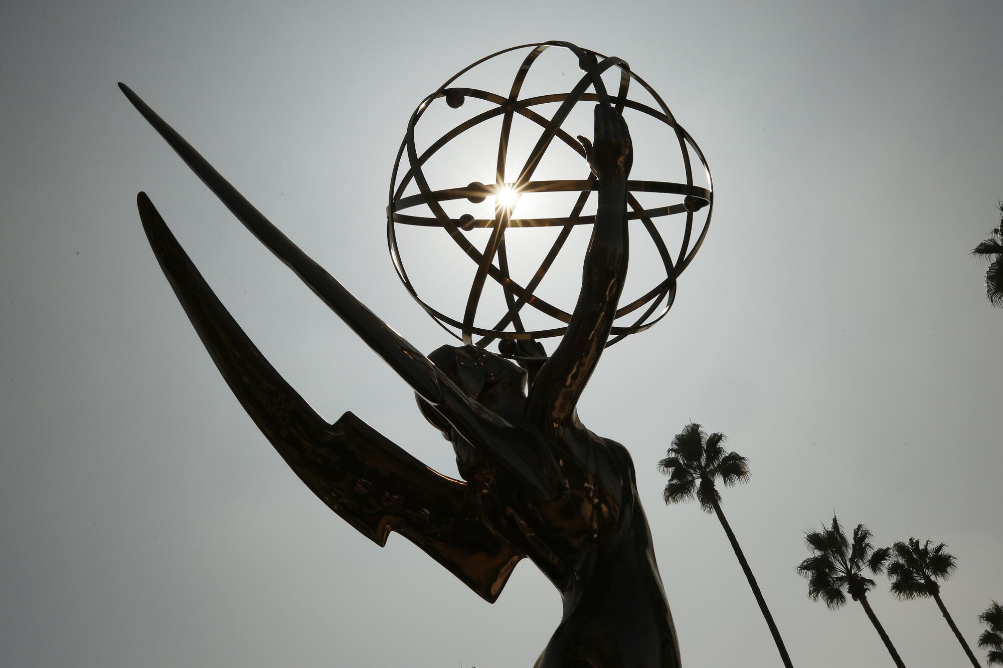 A large Emmy Award statue in silhouette with palm trees in the background