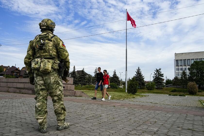 FILE - A young couple walks past a Russian soldier guarding an area at the Alley of Glory exploits of the heroes - natives of the Kherson region, who took part in the liberation of the region from the Nazi invaders, in Kherson, Kherson region, south Ukraine, Friday, May 20, 2022, with a replica of the Victory banner marking the 77th anniversary of the end of World War II right in the background. Ukrainian forces pressing an offensive in the south have zeroed in on Kherson, a provincial capital that has been under Russian control since the early days of the invasion. This photo was taken during a trip organized by the Russian Ministry of Defense. (AP Photo, File)