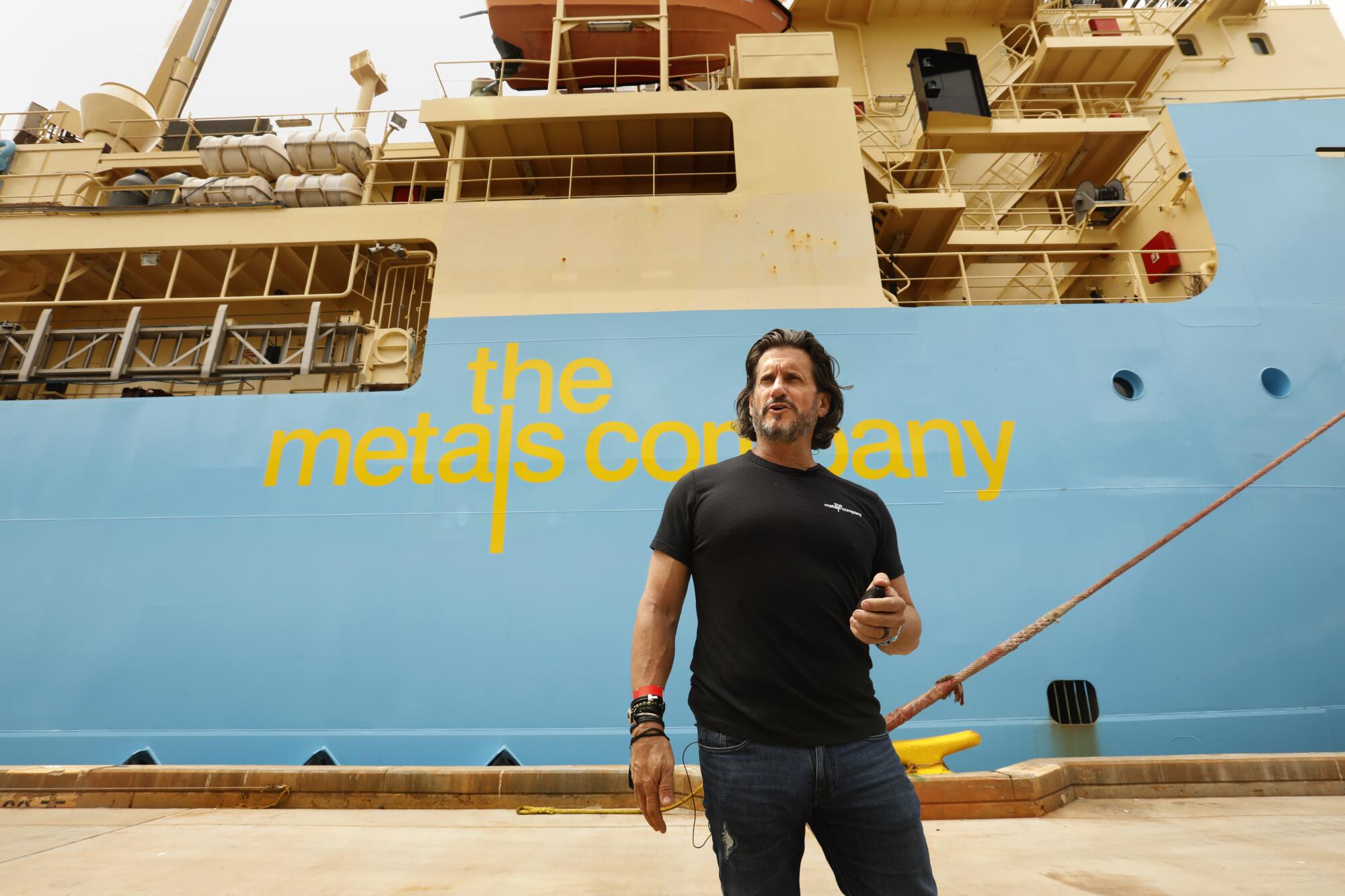 Um homem está diante de um navio atracado que traz um logotipo dizendo: "a empresa metalúrgica."