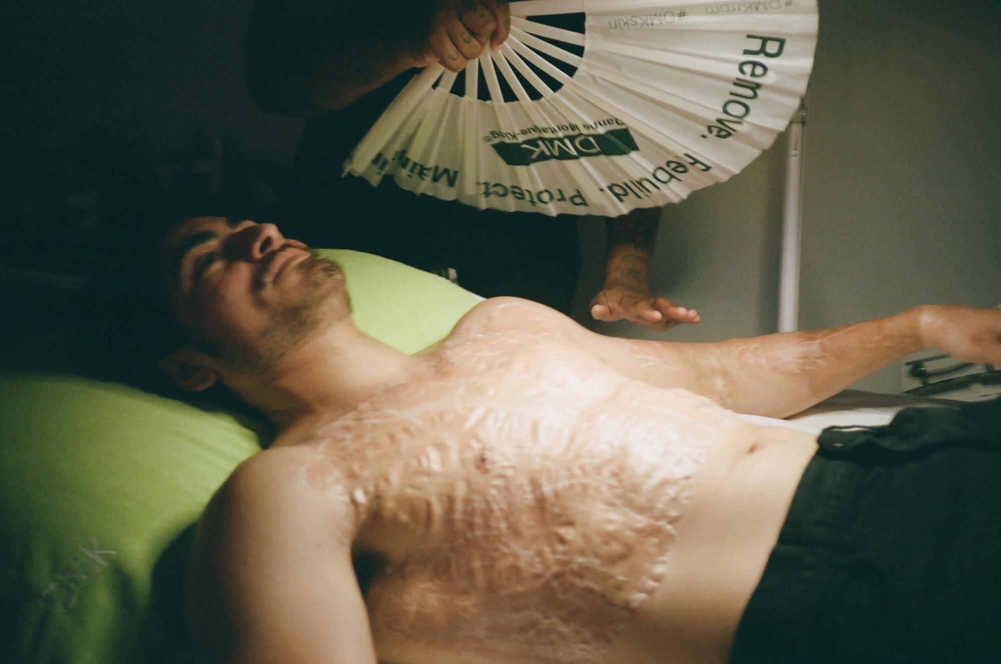 A person lies on a table while another person holds a fan.
