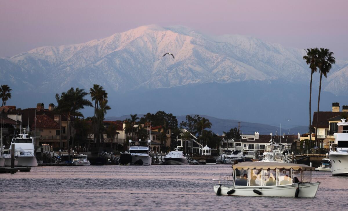 A boat floats near bay front homes with a view of snowy mountains in the distance.