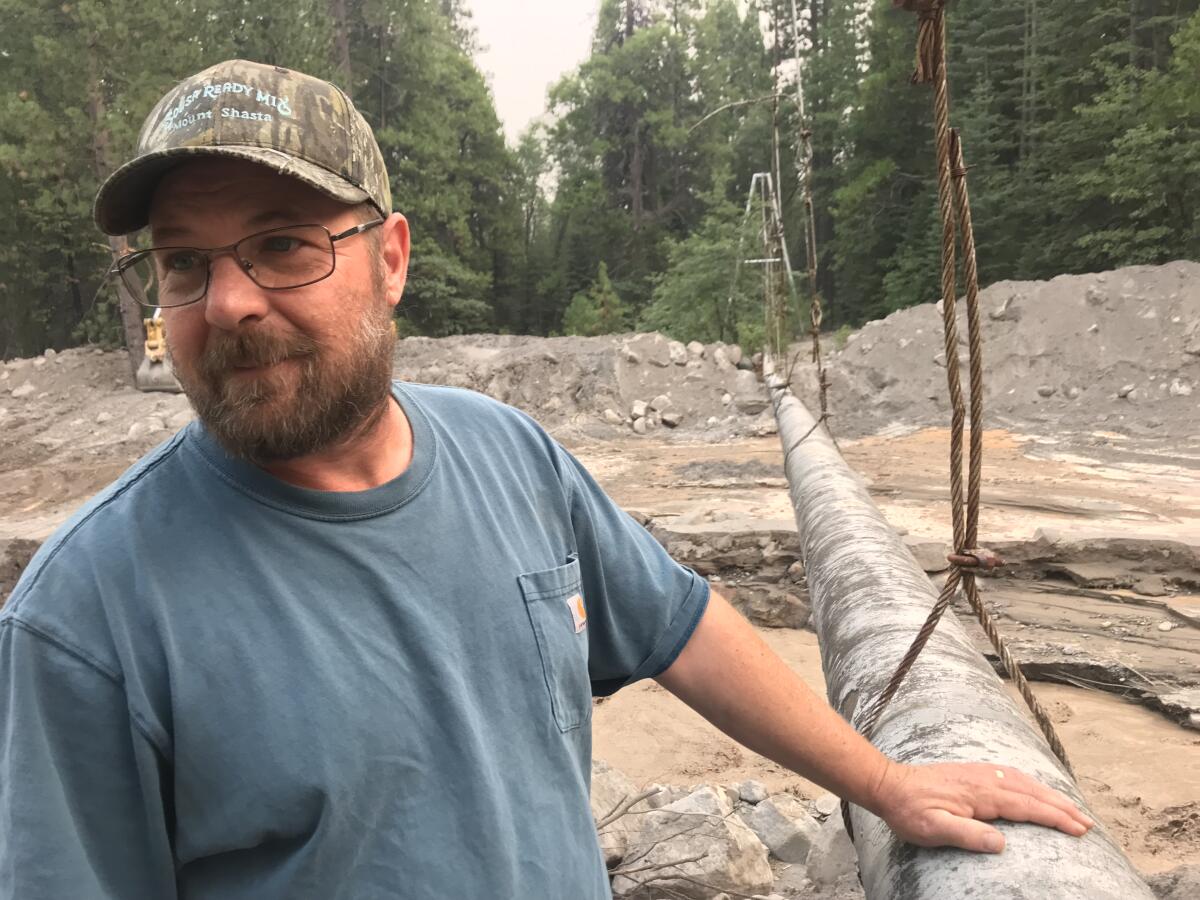 Richie Fesler stands outdoors, his hand on a pipeline and tall pine trees in the background.