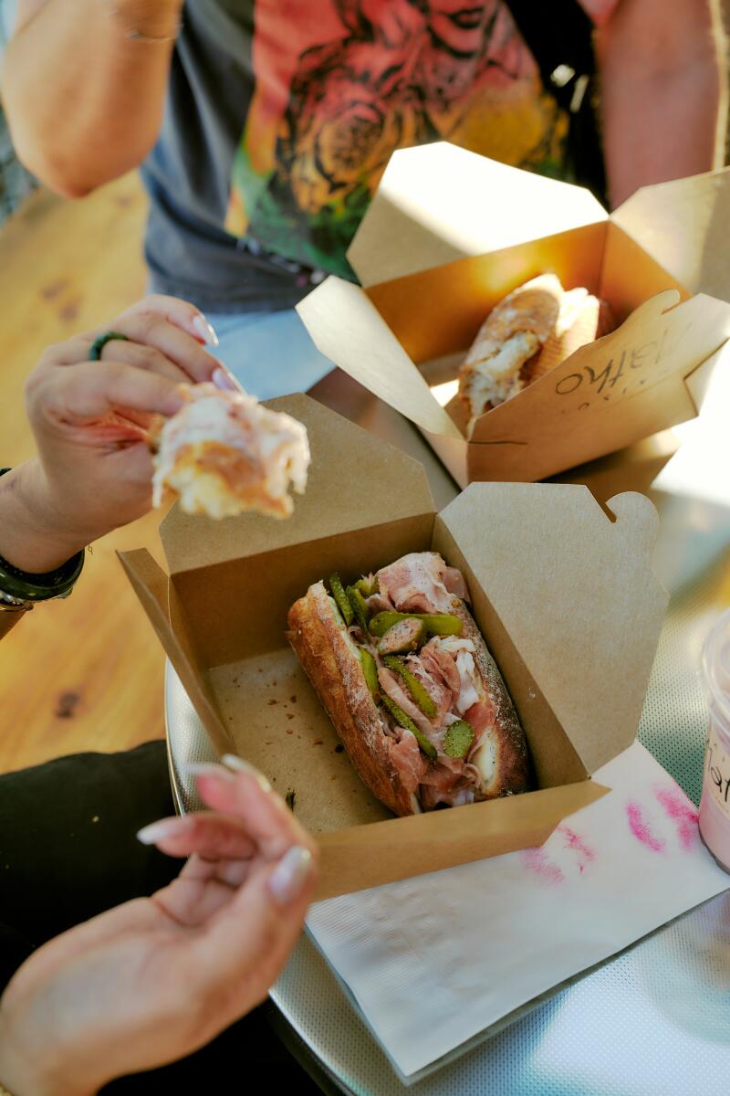 Hands holding cardboard boxes that contain sandwiches.