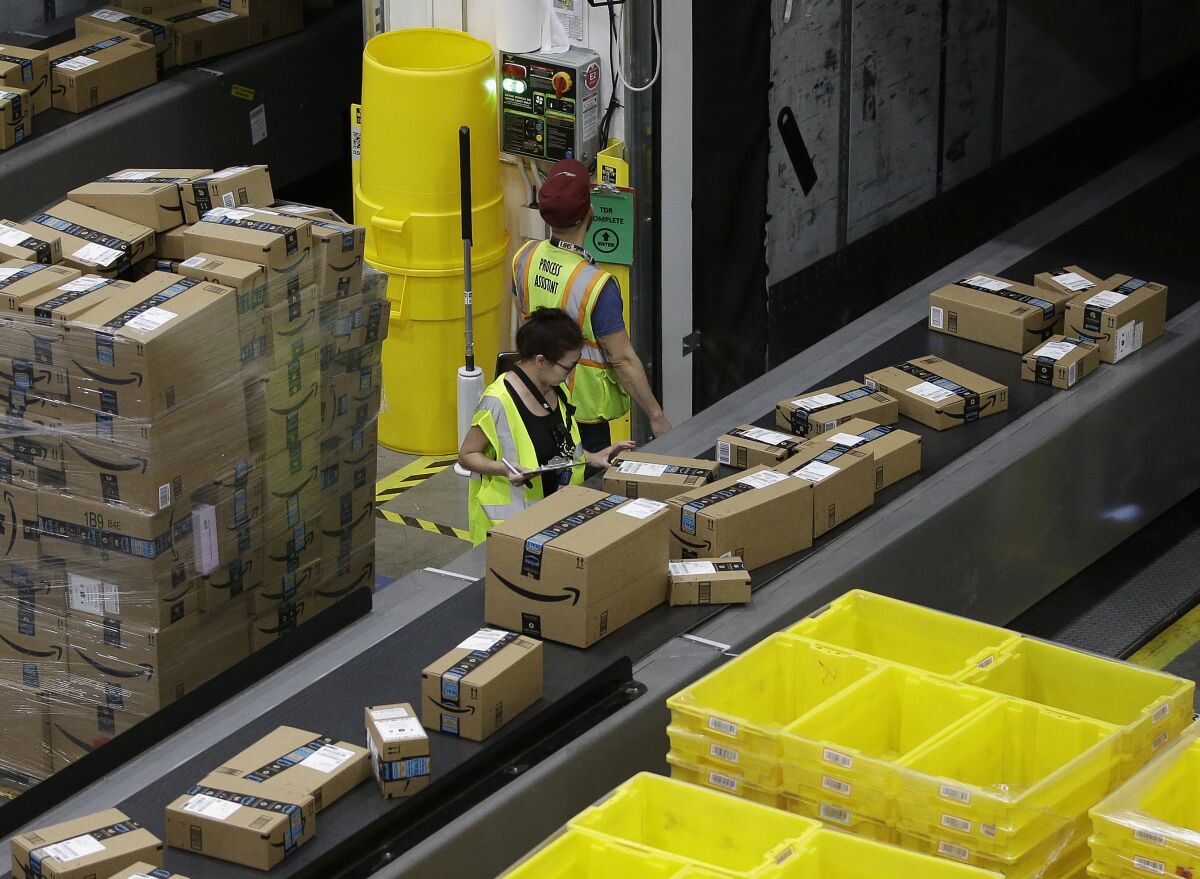 An Amazon workers examines packages on a conveyor belt. 