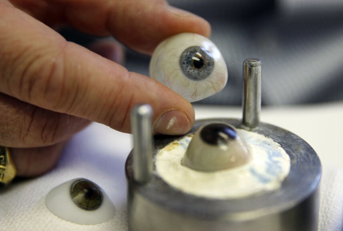 Stolpe holds a finished prosthetic eye next to a eye in the process of being molded.