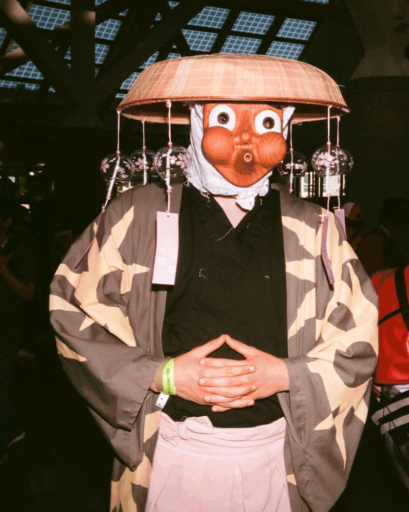 A gif of a person wearing a kimono and a wooden helmet and face mask with puffed out cheeks