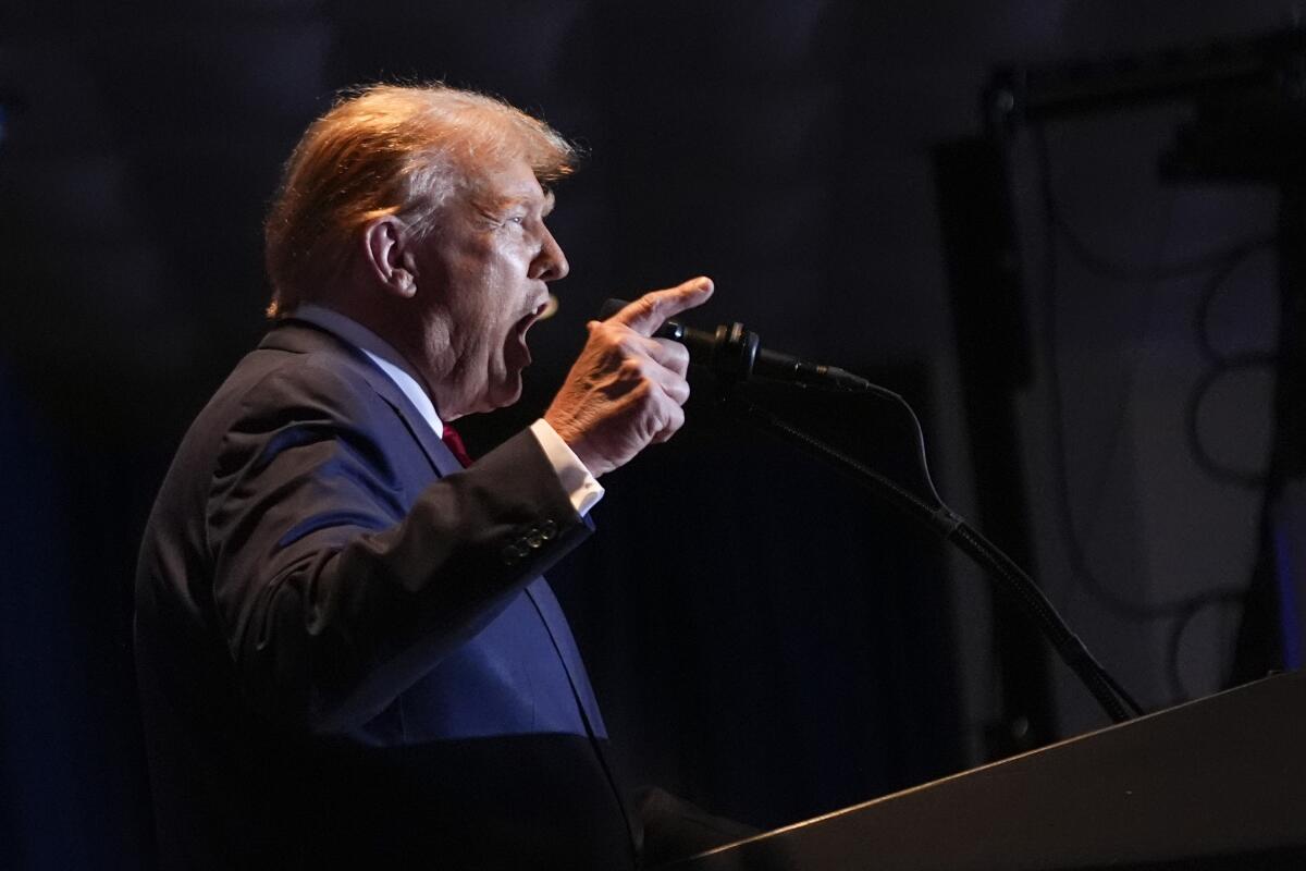 Former President Trump speaks and gestures before a microphone.
