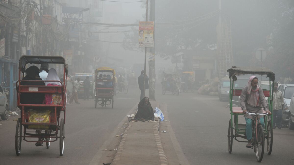 A homeless Indian sits on a road median amid heavy smog in New Delhi.
