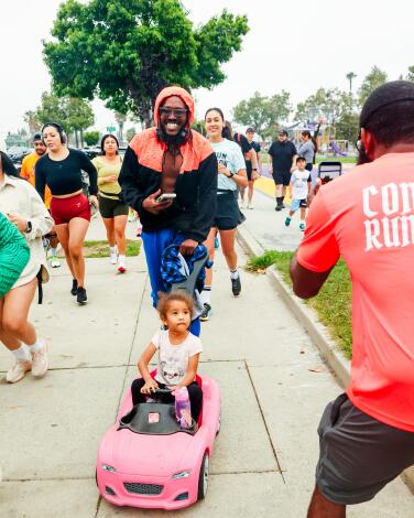 Andrew Johnson runs while pushing a pink car stroller with his daughter Femi Johnson.