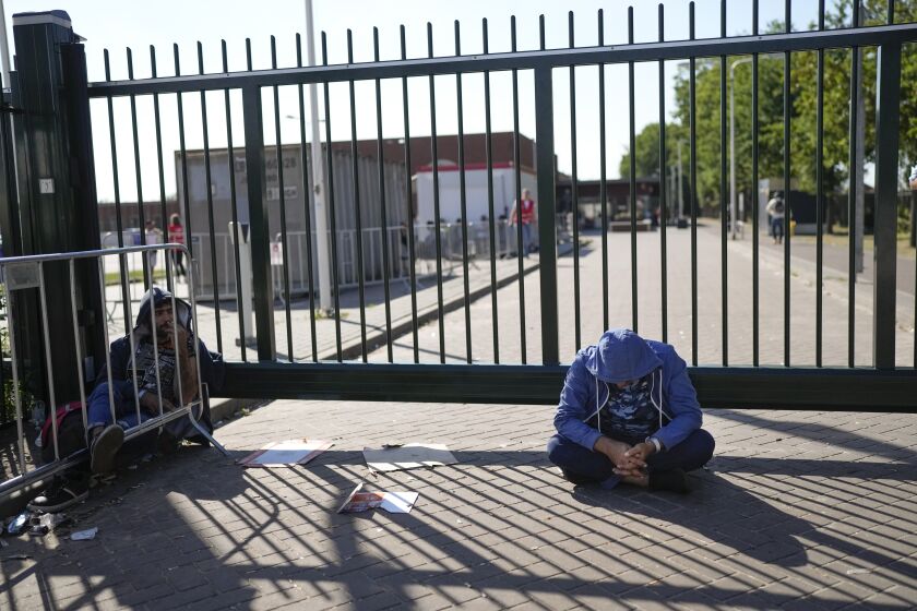 FILE - A man sits outside the gate of an overcrowded asylum seekers center where hundreds of migrants seek shelter in Ter Apel, northern Netherlands, Thursday, Aug. 25, 2022. A Dutch court on Thursday, Oct. 6, 2022 ordered the government and its asylum seeker accommodation agency to significantly improve conditions at overcrowded and unsanitary emergency migrant housing facilities. (AP Photo/Peter Dejong, File)