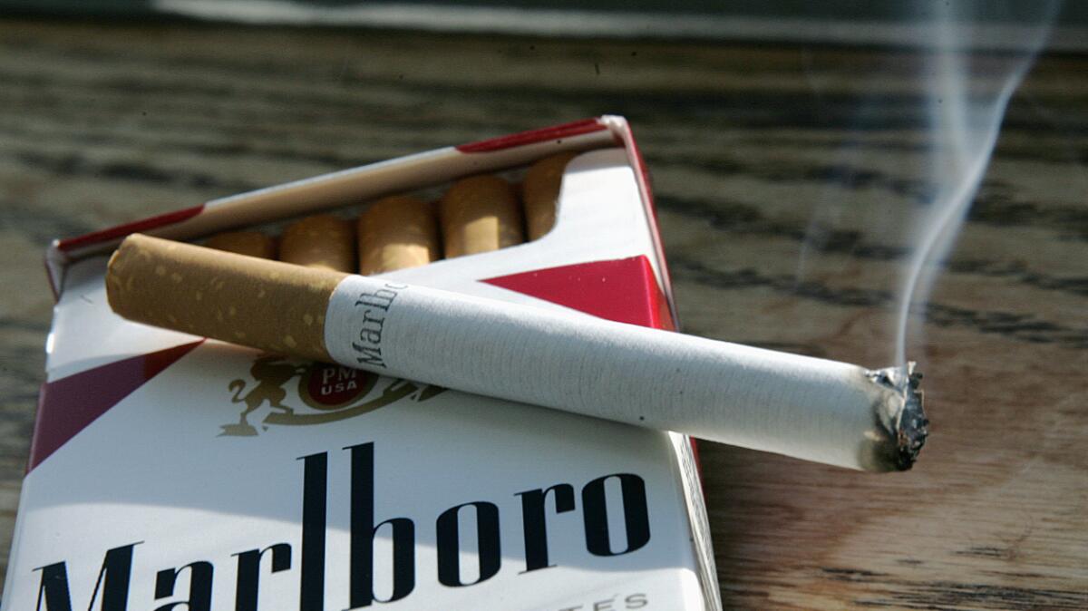 A cigarette burns on top of a pack.
