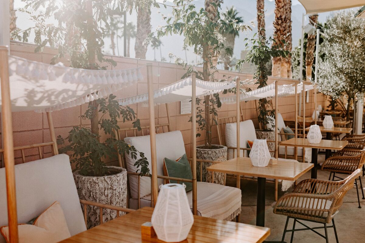 Tables and chairs under fabric shades on an outdoor patio at a restaurant