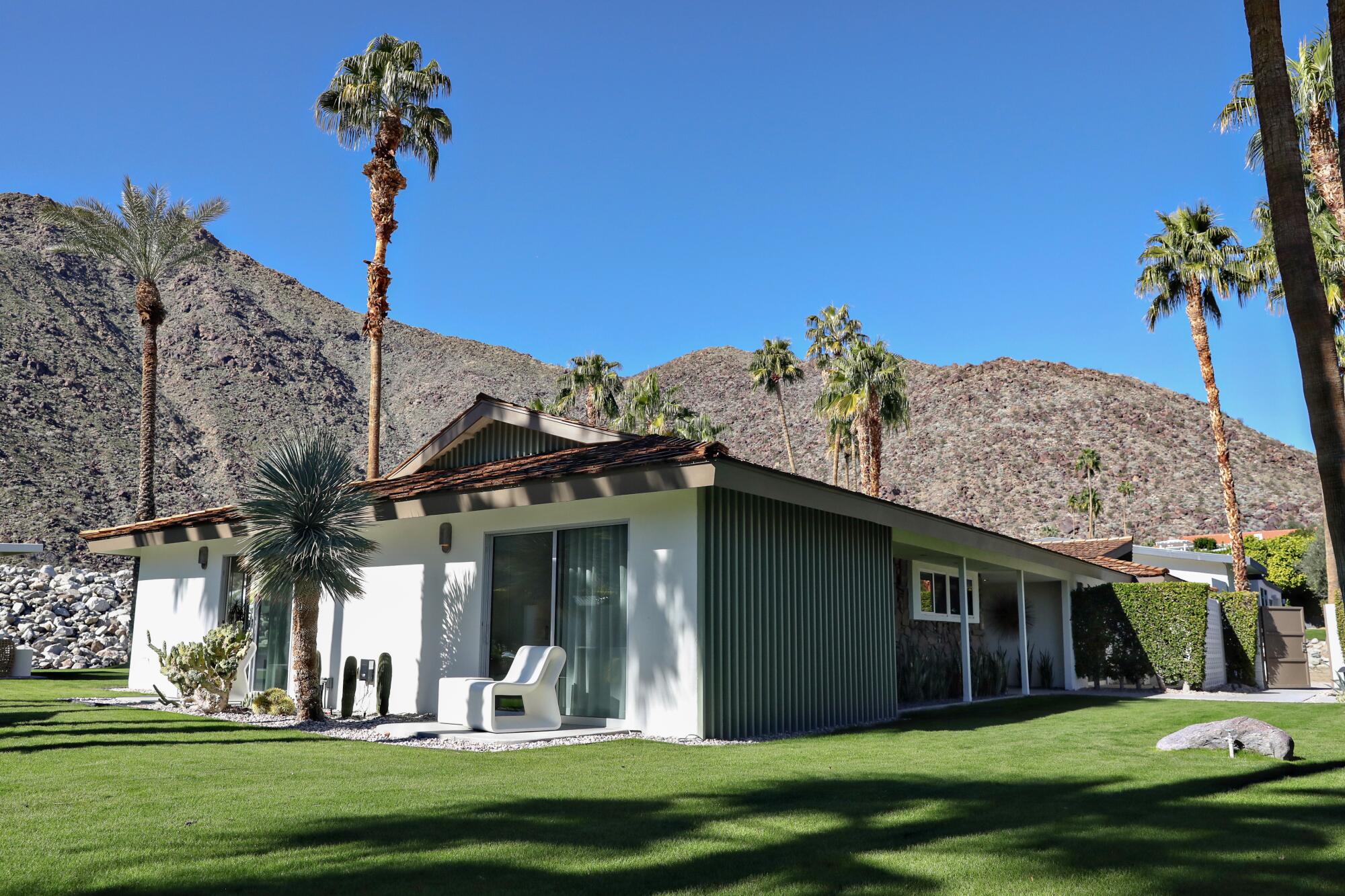 Exterior of a Midcentury Modern home set amid grass and palm trees, with mountains in the background