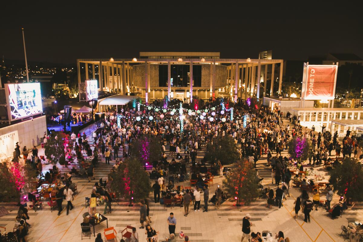 A crowd gathers on a plaza in front a lighted building