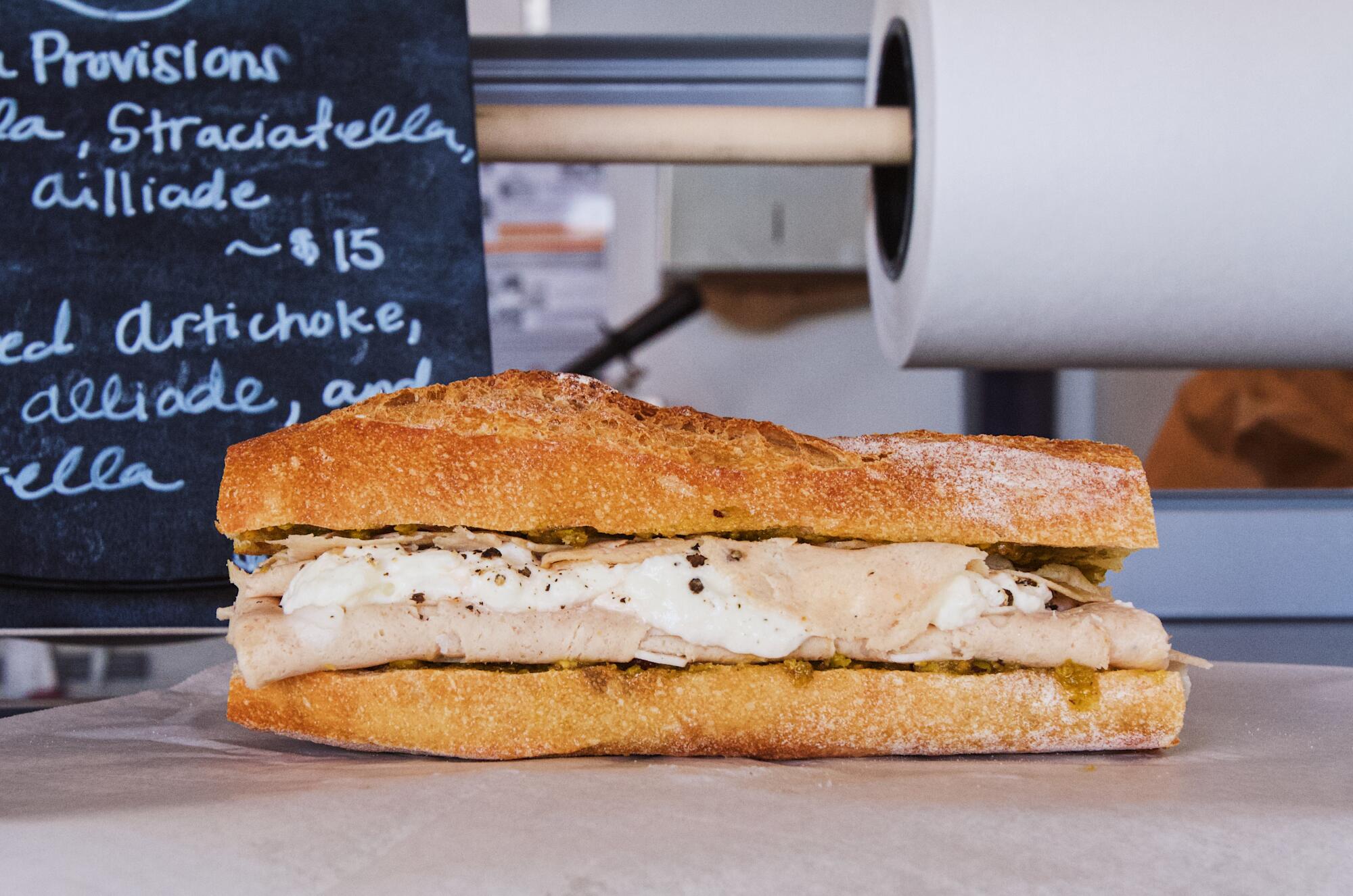 A horizontal photo of a mortadella sandwich resting on butcher paper atop a deli counter