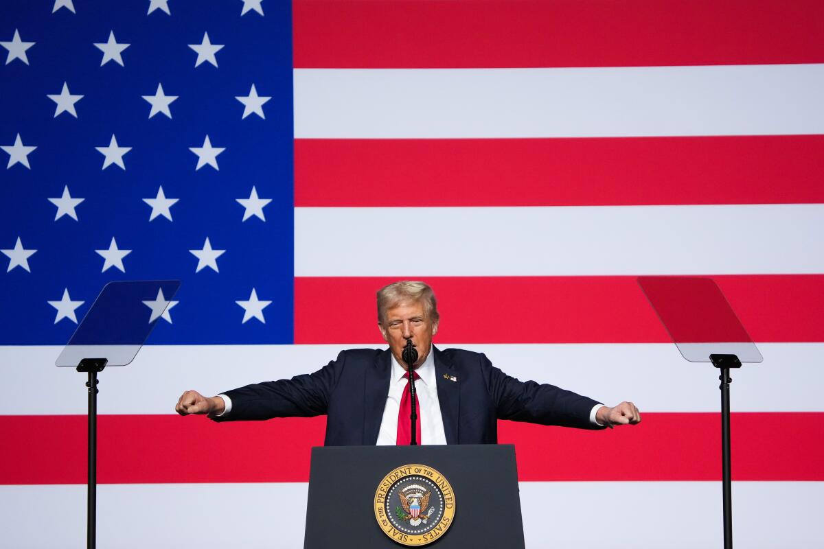 A man at a lectern with a giant American flag behind him.