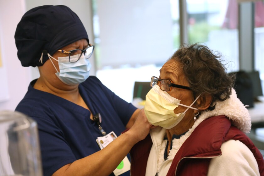 Maria Saravia of USC's Keck Hospital tightens her mother's mask before her mother receives the COVID-19 vaccine.