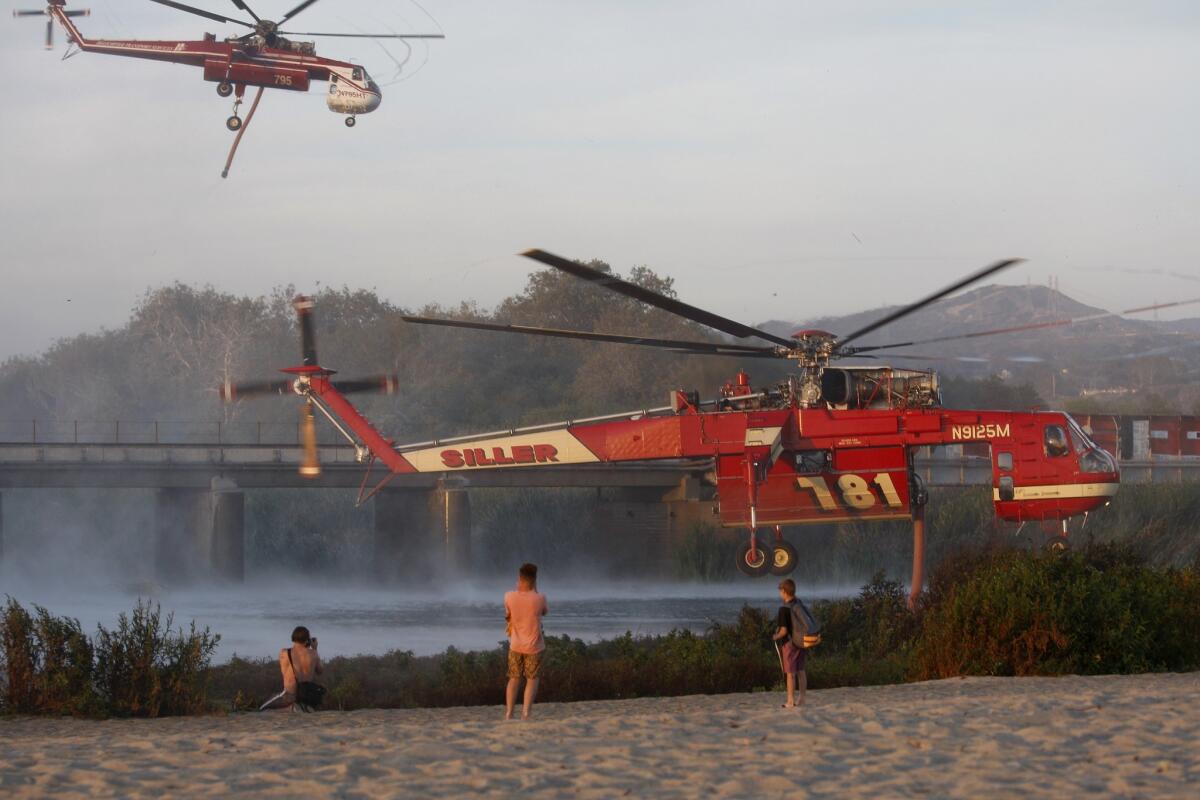 People watch from Trestles beach in San Clemente as firefighting helicopters suck water from a lagoon to fight the San Mateo fire at nearby Camp Pendleton.