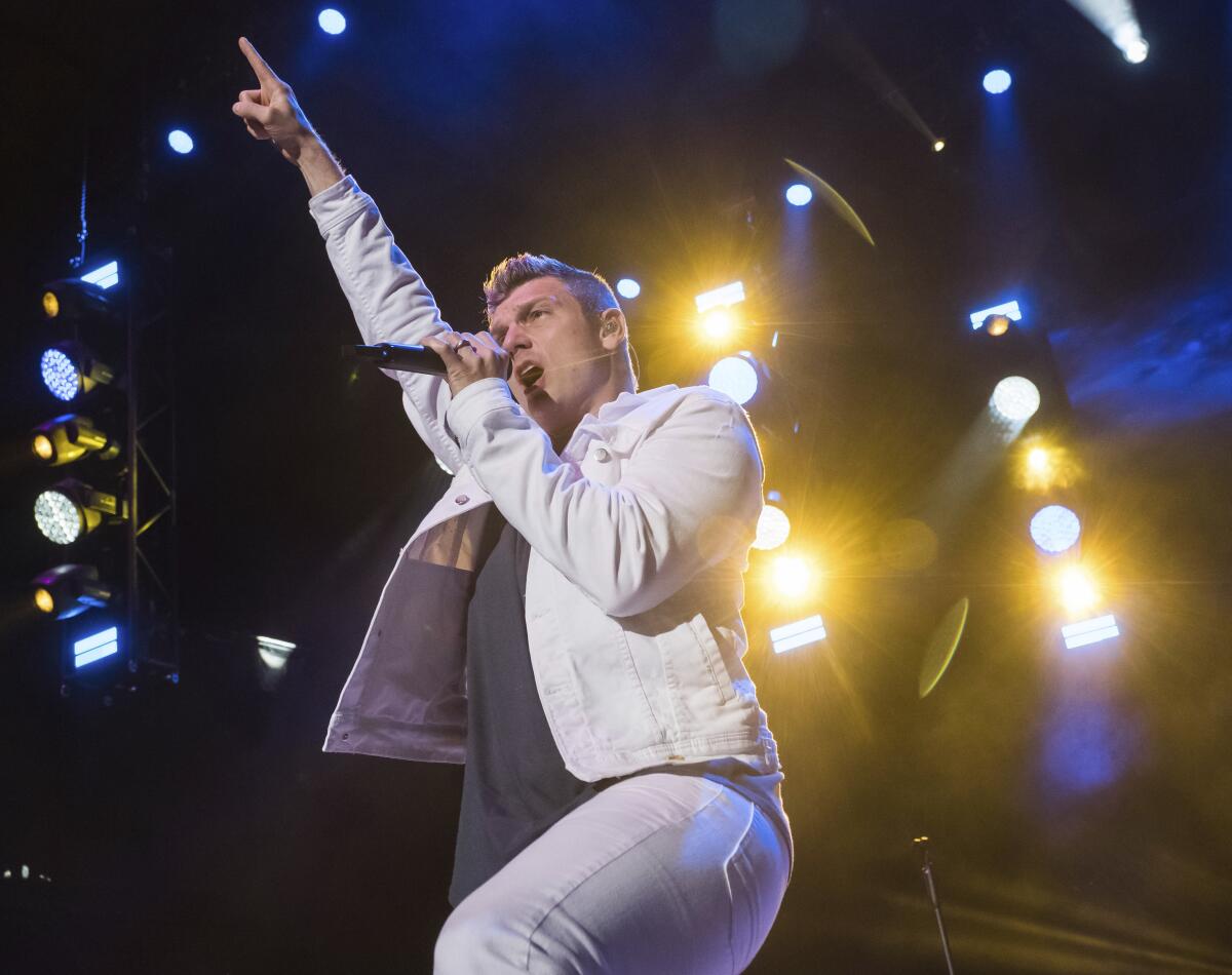 Nick Carter sings onstage in a white jacket and pants and points one finger to the sky