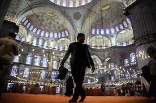 A man walks in a domed room with grand arches and stained glass windows