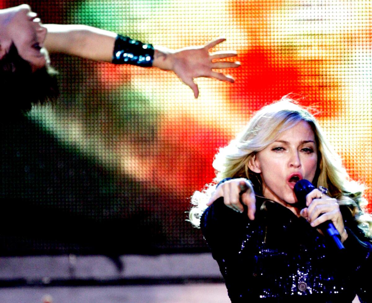 Madonna sings into a microphone onstage and points toward the audience