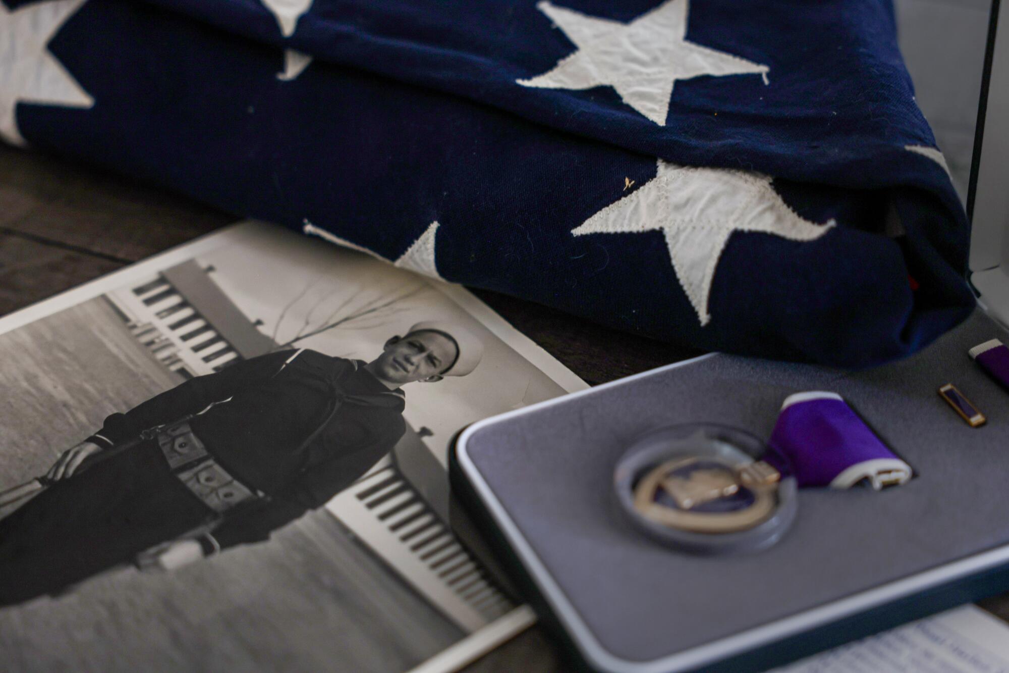 A black and white photograph of a sailor in uniform, a folded flag and a Purple Heart medal