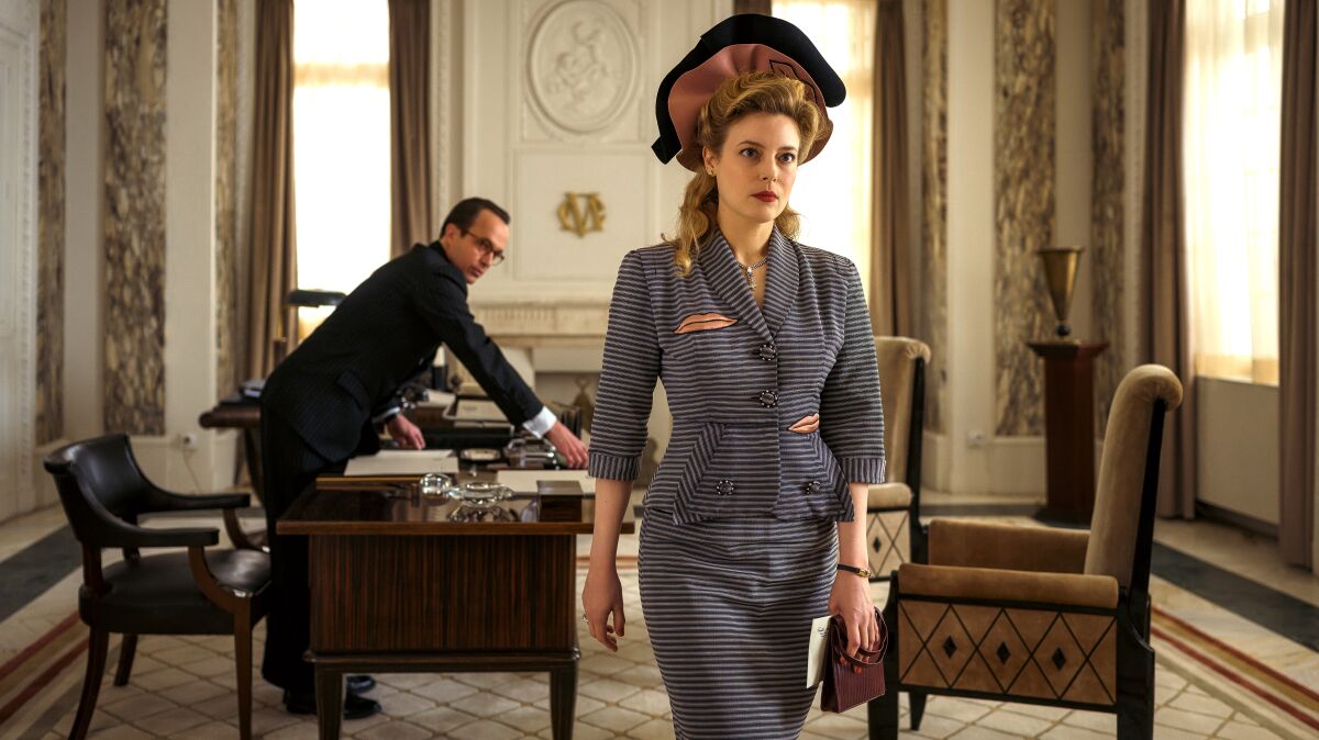 A woman in 1940s fashion walks out of an office in a scene from "Transatlantic."