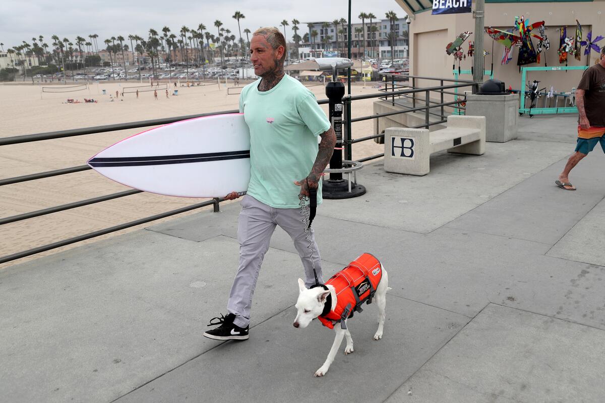 Trainer Ryan Rustan and his dog Sugar walk along the Huntington Beach Pier on Friday.