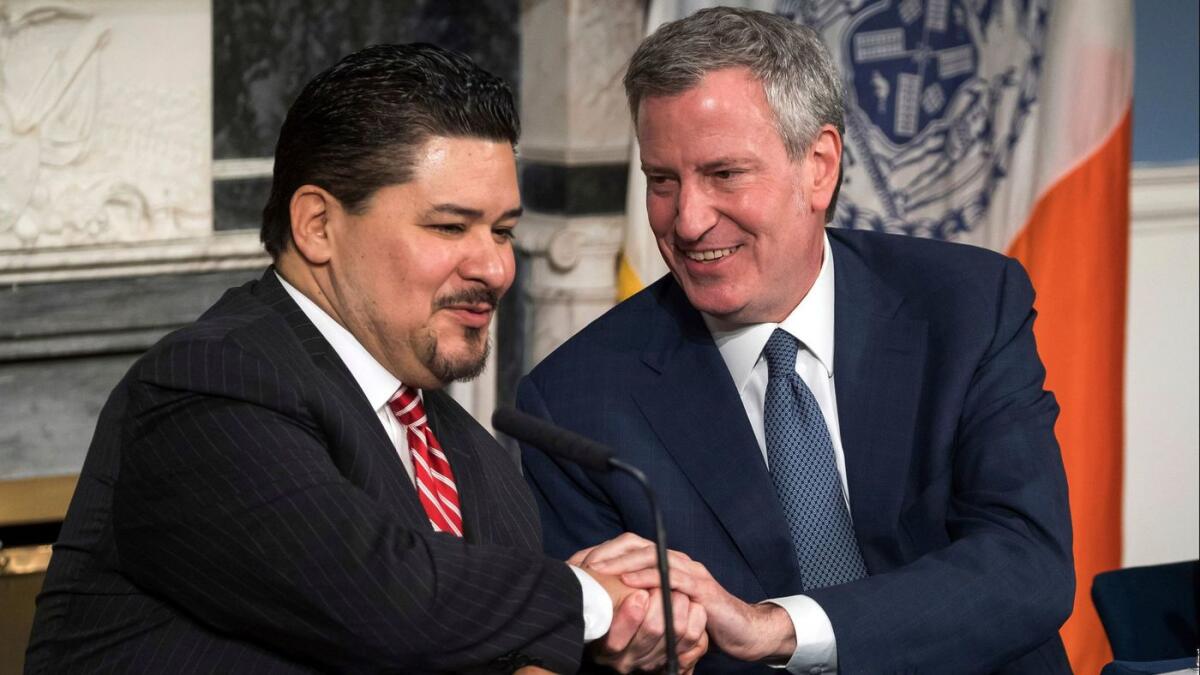 New York Mayor Bill de Blasio, right, holds tight to this one as he welcomes Richard A. Carranza.