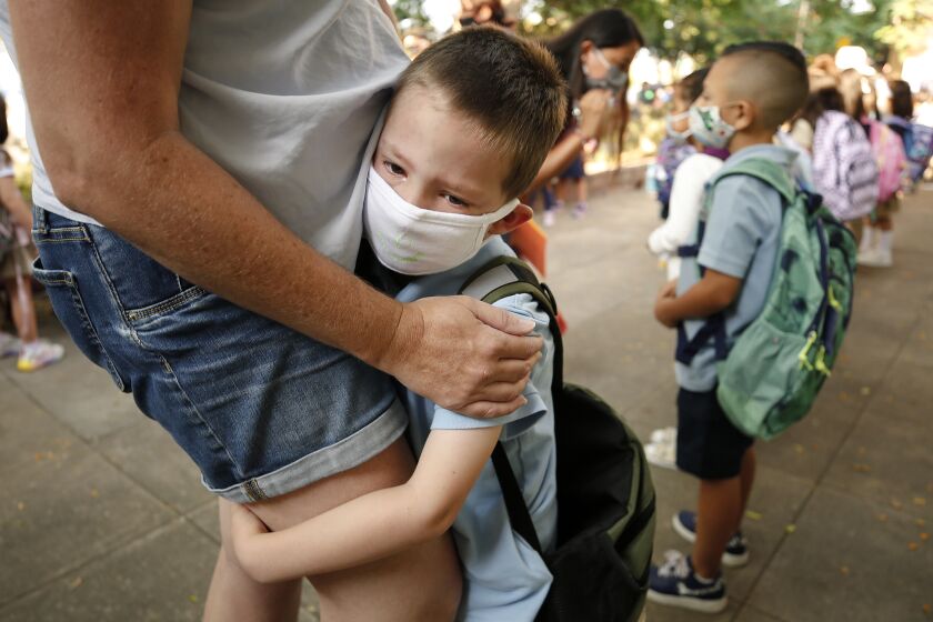 ALTADENA, CA - AUGUST 12: Kindergarten student August Russell clings to the leg of his Mother Natalie Russell as she tries to comfort him for his first day in a classroom as parents say good bye as they deliver their students to teachers for the first day of school for PreK - 5th Grade students at Jackson STEM Dual Language Magnet Academy in Altadena. For the kindergarten and first grade students it will be their first time in a classroom. Jackson STEM Dual Language Magnet Academy on Thursday, Aug. 12, 2021 in Altadena, CA. (Al Seib / Los Angeles Times).