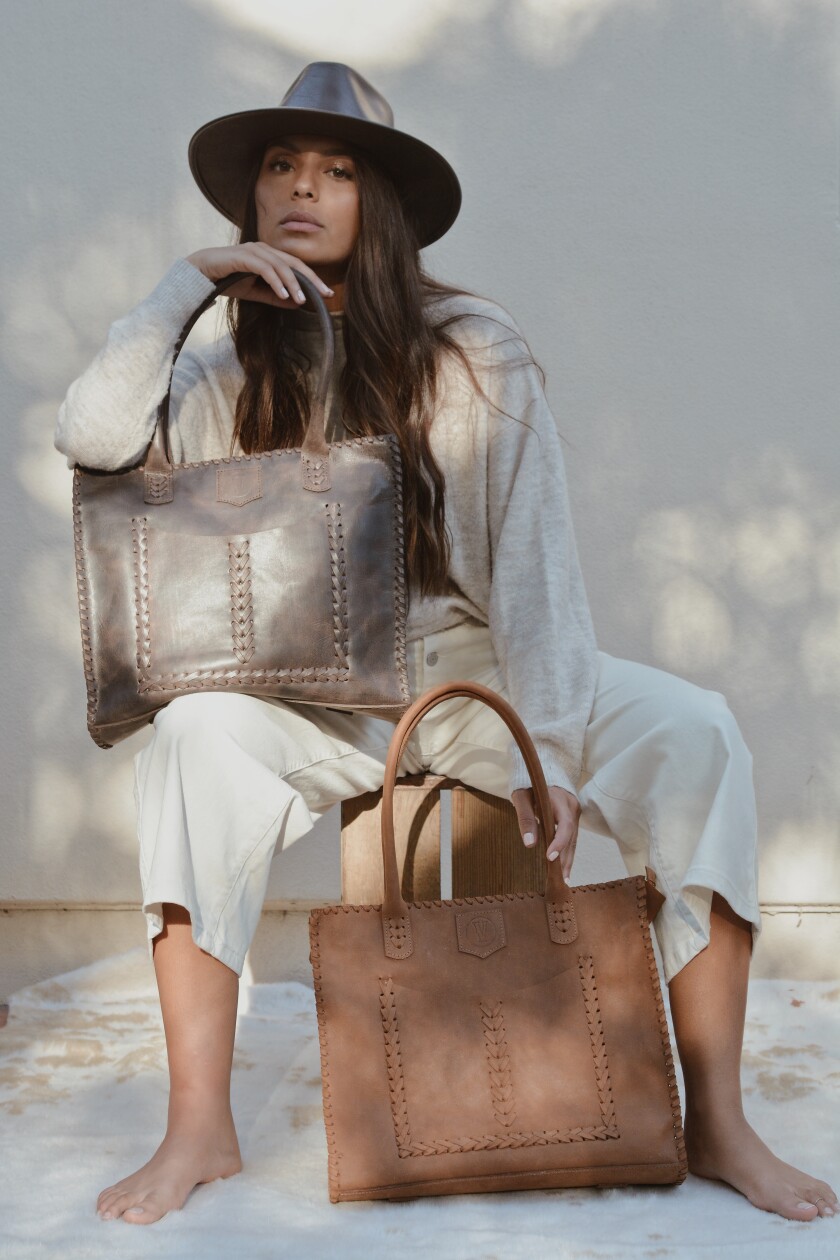 A seated woman holding two large leather bags.