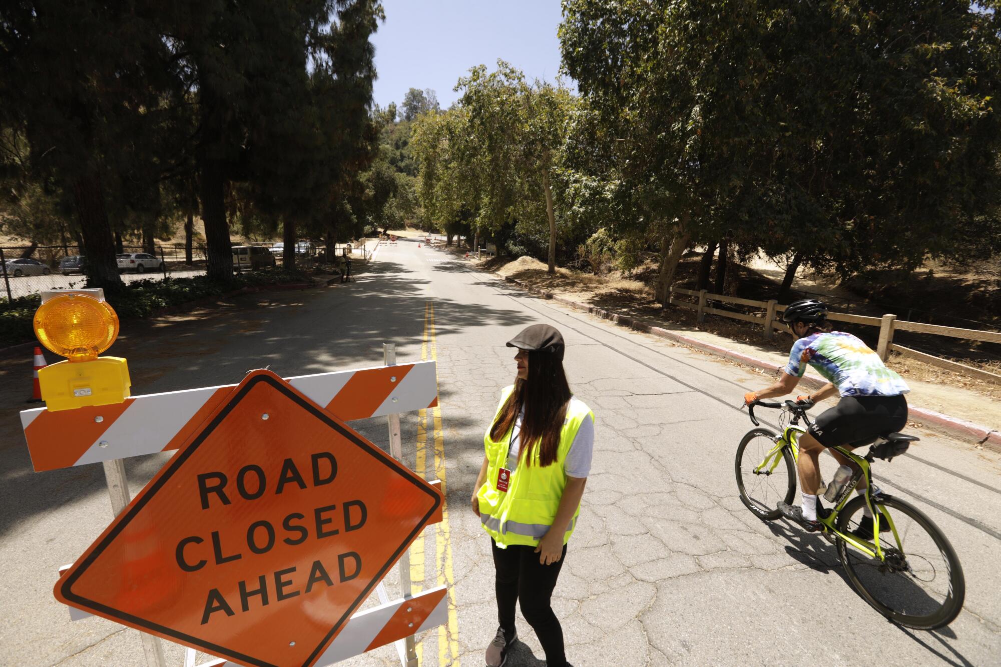 A cyclist rides past a worker who is standing next to a sign that reads, "road closed ahead."
