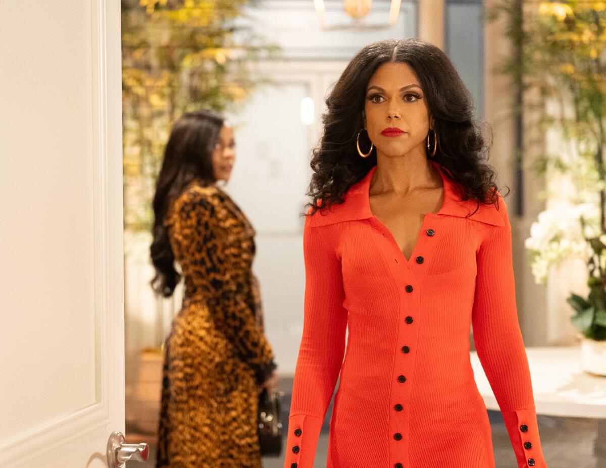 A woman with a tight long -sleeved orange dress with black buttons in the middle walking through a door.
