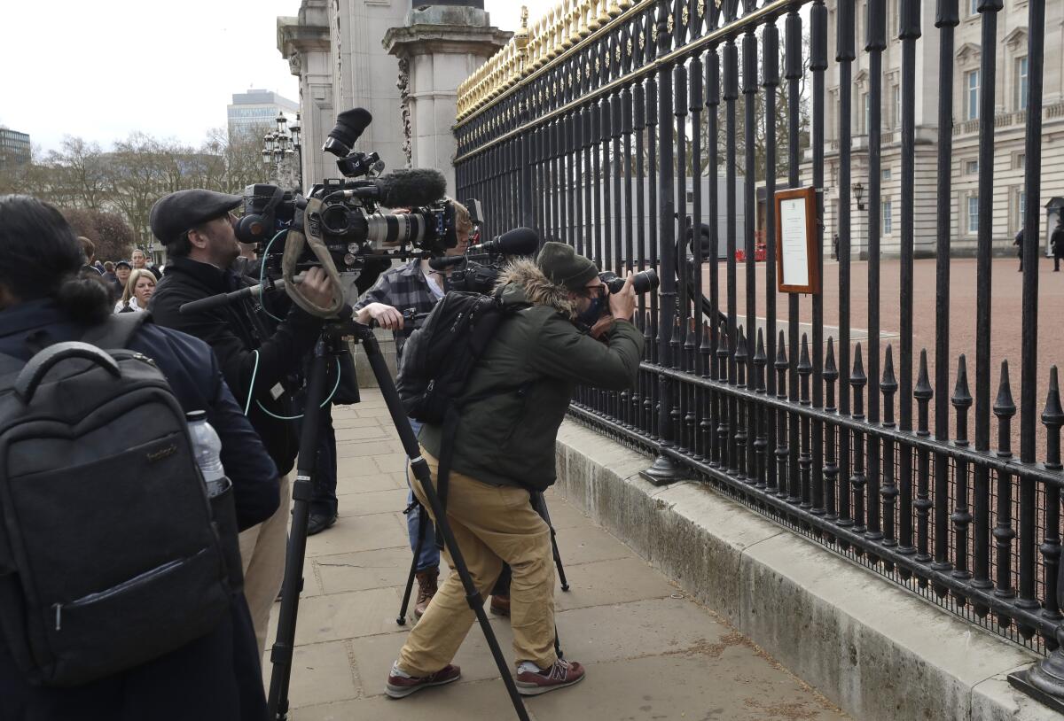 FILE - In this Friday, April 9, 2021 file photo, members of the media take images of an announcement, regarding the death of Britain's Prince Philip, displayed on the fence of Buckingham Palace in London. When Prince Philip’s death was announced, the BBC switched instantly into mourning mode. Regular programming on the U.K.’s national broadcaster was canceled for special coverage, hosted by black-clad news anchors. Some Britons felt it a fitting mark of respect, but for others it was a bit much. (AP Photo/Matt Dunham, File)