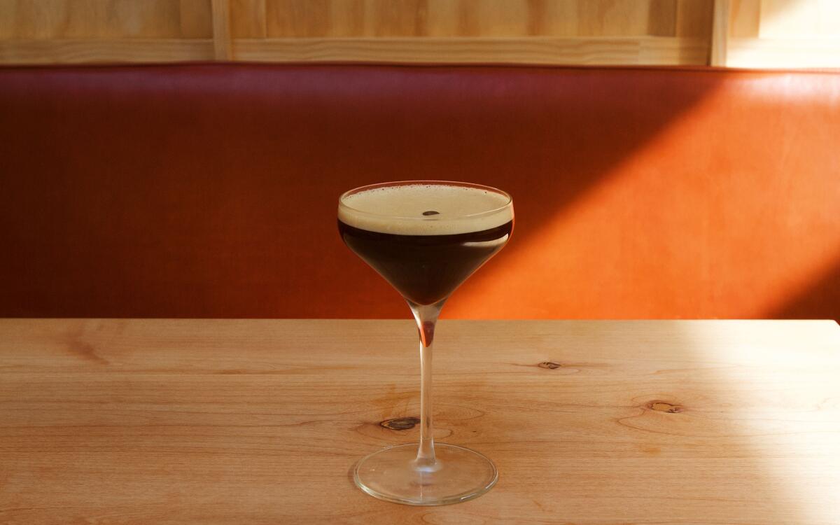 A nonalcoholic espresso martini adorned with a layer of foam and an espresso bean on a wood table at Highly Likely