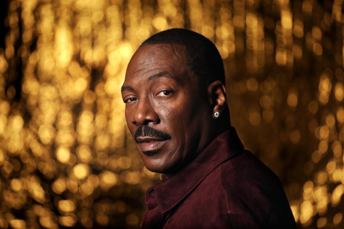 Eddie Murphy stands in front of a sparkly gold background.
