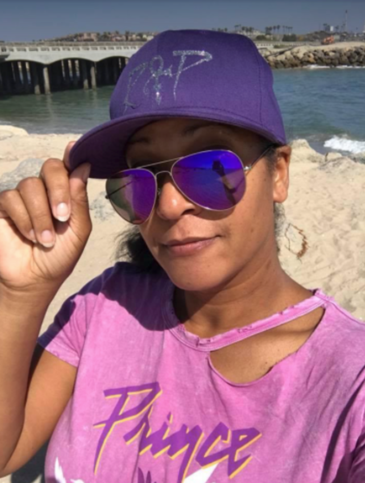 Woman wears purple Prince apparel and purple sunglasses on the beach 