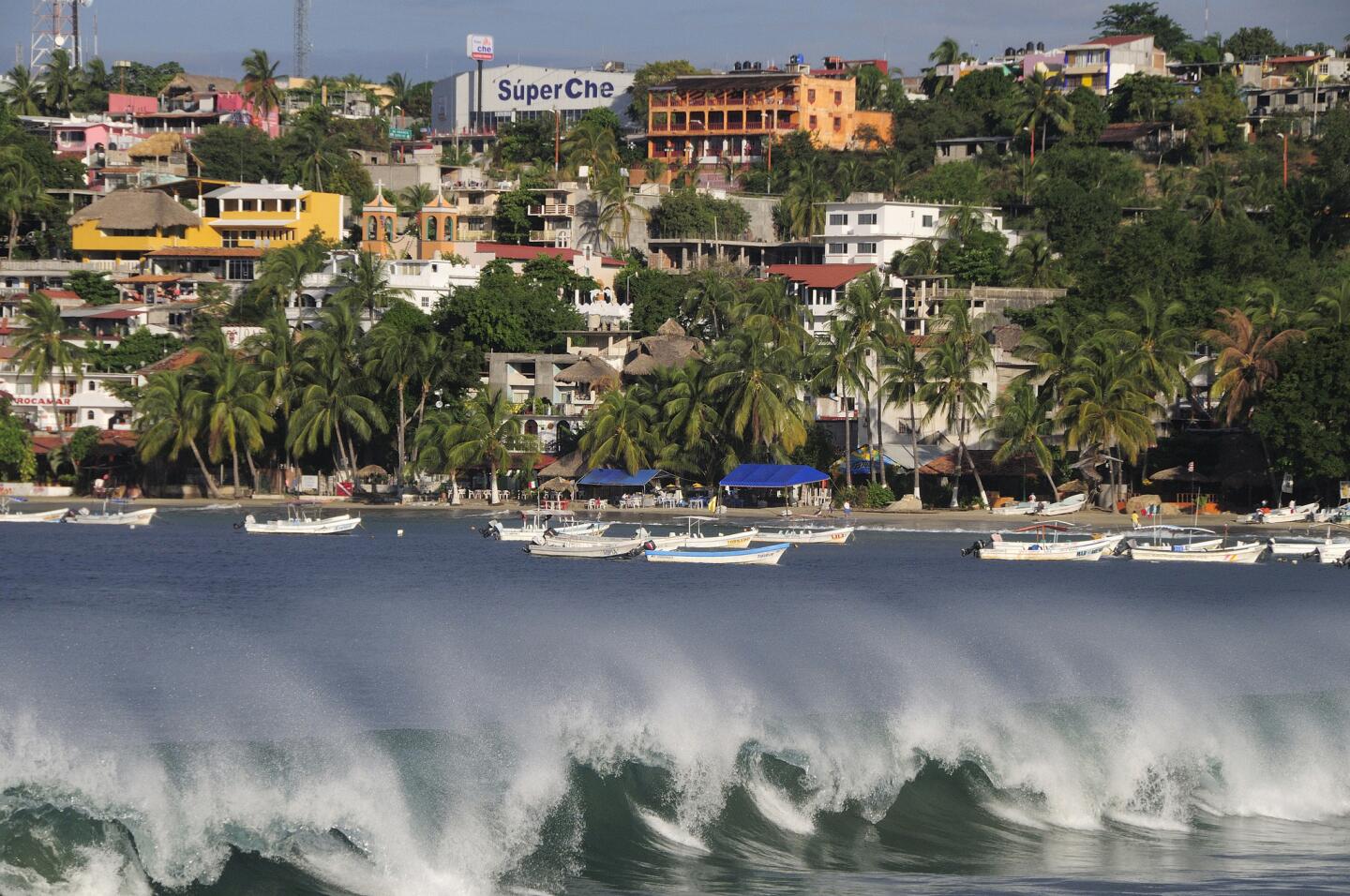 Colorful buildings overlook breaking waves and boats along Playa Principal in Puerto Escondido.