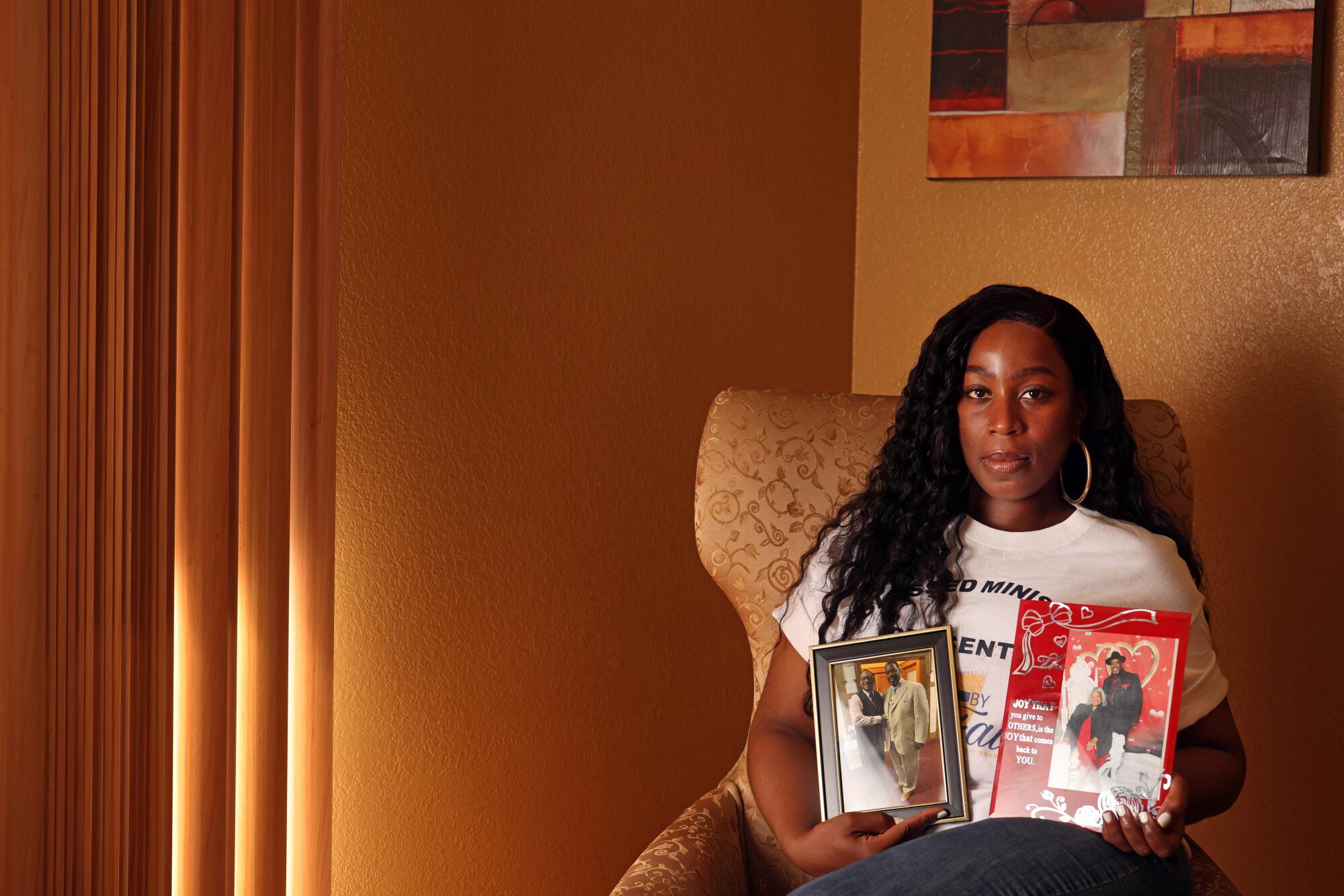 A woman sitting in a chair holds two framed photographs