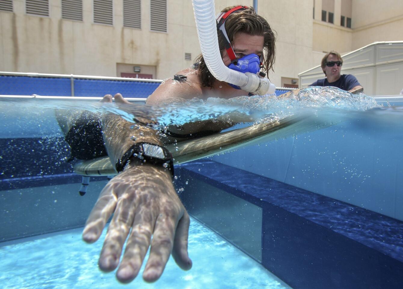 While wearing a mask, to measure oxygen consumption, kinesiology student Cody Cuchna, 24, paddles a surfboard against the current created in a swim flume as Assistant Professor Sean Newcomer watches.