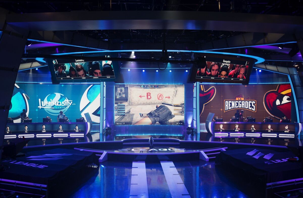 A screen, center, shows a professional video game competition between teams sitting on either side. Unionization of players is a big topic in the industry after several years of fast growth.