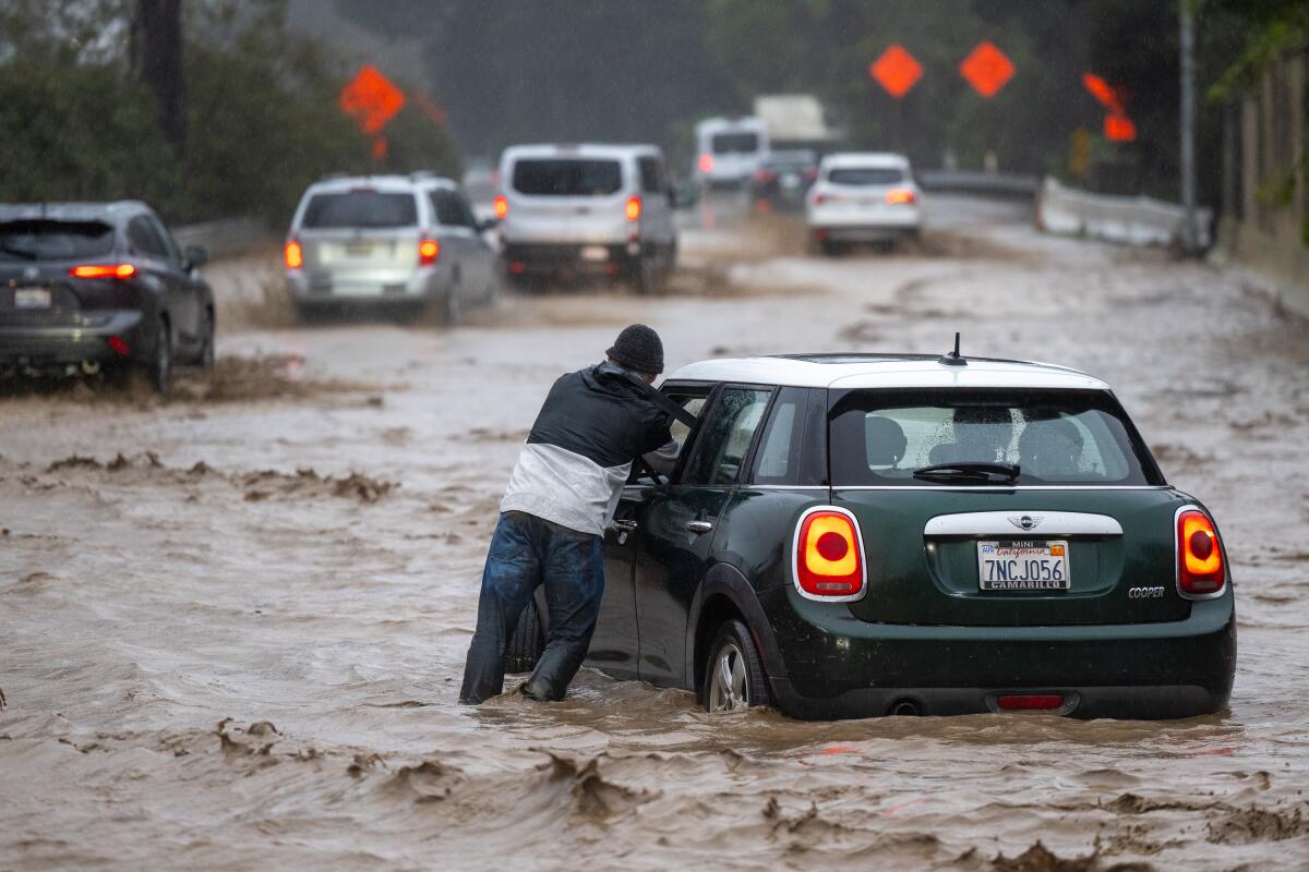 A man pushes his stalled car from the southbound 101 Freeway in Montecito during a heavy downpour.