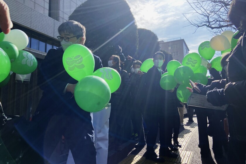 Partidarios de seis personas que denunciaron a la empresa que gestiona la plata de Fukushima tras desarrollar cáncer de tiroides luego del accidente nuclear, esperan con globos verdes en el exterior del Tribunal de Distrito de Tokio, el 27 de enero de 2022. (AP Foto/Mari Yamaguchi)