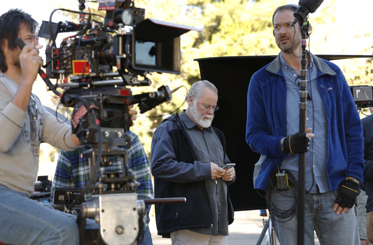 A man with a movie camera, a man looking at his phone and a man holding a boom mic on a movie set